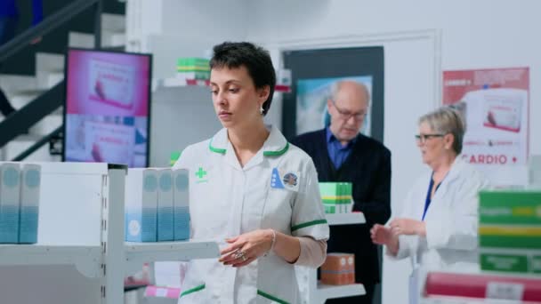 Přátelský Lékárník Lékárně Umísťuje Krabici Pilulkami Police Zatímco Starší Spolupracovník — Stock video