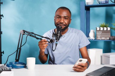 Akıllı telefondan ve çevrimiçi portreden okurken mikrofonla konuşan neşeli bir vlogger. Gülümseyen blogcu, abonelerin sorularını yanıtlıyor ve sosyal medya kanalı için canlı yayın yapıyor