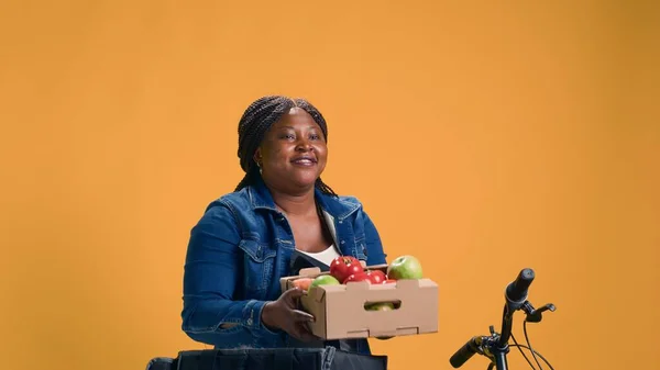 Fruit basket being gently carried out of food delivery bag by african american bike messenger. Female african american courier riding bicycle while grinning as she delivers fresh produce.