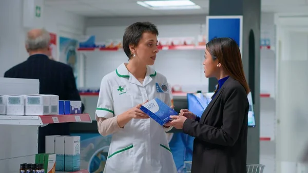 stock image Knowledgeable pharmacist in drugstore with patient prescribing her melationin pills to cure sleeping trouble. Asian client receiving insomnia medical product from chemist shop employee