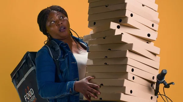 African american delivery person balancing plenty of pizza boxes for delivering to neighborhood. Active black woman on bicycle carefully carrying a big food order for transportation.