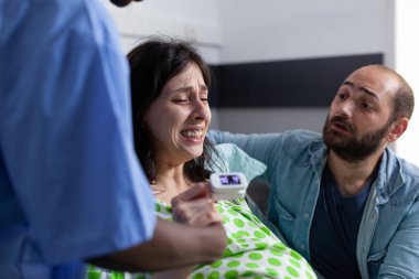 Hastane koğuşunda hemşire ve kocanın elini tutan hamile bir kadın. Ağrılı kasılmalar geçiriyor. Hamileliği olan bir hasta, sağlık merkezinde tıbbi yardım alıyor. Kapat.