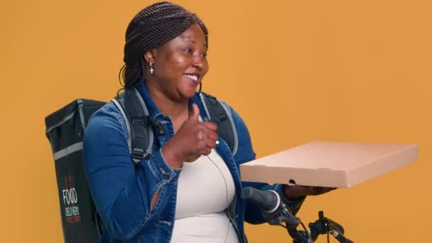 骑自行车的黑人妇女从餐馆带来包裹 提供及时可靠的送货服务 美国黑人信使带着外卖盒和大拇指确保了环保食品的运送 — 图库视频影像