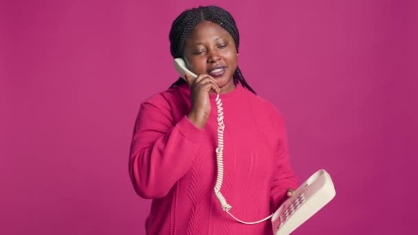 穿着时髦服装的非洲裔美国女人通过手机交谈 女性时尚博主在孤立的粉色背景前 用固定电话交谈 — 图库视频影像