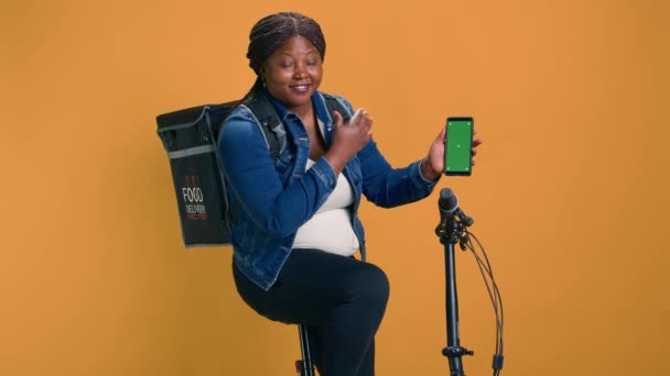 バックパック付きのアフリカ系アメリカ人女性は 孤立した緑色の画面ディスプレイでスマートフォンを運ぶ フレンドリーな宅配業者は 染色体モックアップテンプレートを使用した携帯電話のオンライン注文ロジスティクスを示しています — ストック動画