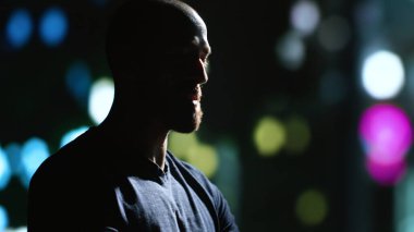 Genç yetişkin gece şehir merkezinde geziniyor, sokak lambalarının altında akıllı telefon kullanarak gökdelenlerin yakınında yürüyor. Şehir merkezinde mesaj atmaktan zevk alan bir adam. El kamerasıyla. Kapat..