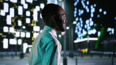 Yetişkinler gece gökdelenlerin etrafında dolaşır sokak lambalarının altında şehir merkezinde dolaşır. Afrika kökenli Amerikalı iş adamı gece yarısı gezinti güvertesinde şehir merkezinde dinleniyor. El kamerasıyla..