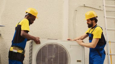 Ekip çalışması öngörülebilir mühendis arızalı Hvac sistemi üzerinde çalışmaya başlıyor, yoğunlaştırıcı bobin panelini ayırıyor. Hatalı kabloları kontrol etmek için hava aksesuarı açan hassas kablocular.