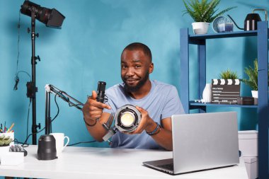 İnternet etkileyicisi video incelerken stüdyo yıldırım ekipmanları tavsiye ediyor. Gülümseyen Afro-Amerikan blog yazarı ürünü internette tanıtırken videografi aracını işaret ediyor