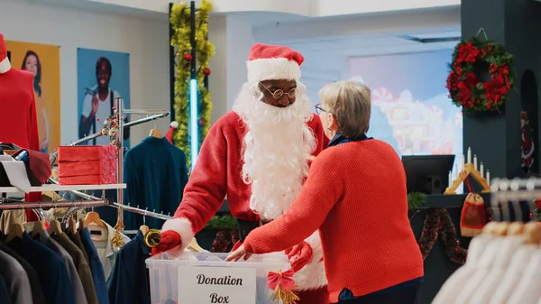 零售助理装扮成圣诞老人 在捐赠箱中从顾客那里收集不需要的衣服 在圣诞期间作为礼物送给那些有需要的人 传播节日欢乐 — 图库照片