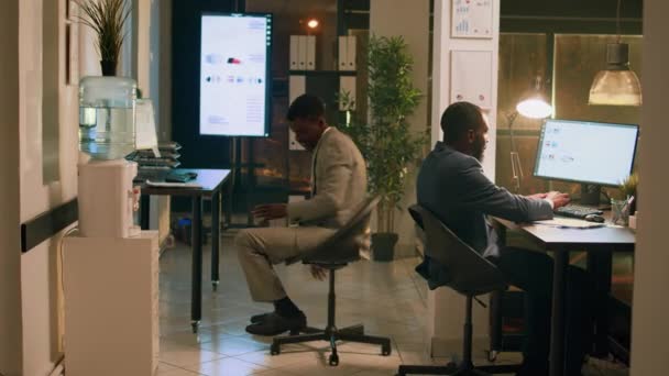 アフリカ系アメリカ人の従業員は 夜勤中に仕事を楽しみ 机の椅子でレースを開催しています オフィスで一晩滞在し 一緒に遊んでいるリラックスしたコワーキングビジネスマン — ストック動画