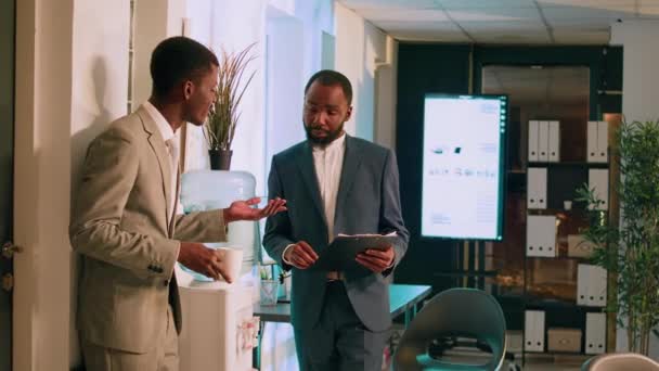 非裔美国人商业经理在夜班期间检查员工项目的进度 放松办公室职员在水箱边与主管聊天 喝着一杯咖啡 — 图库视频影像