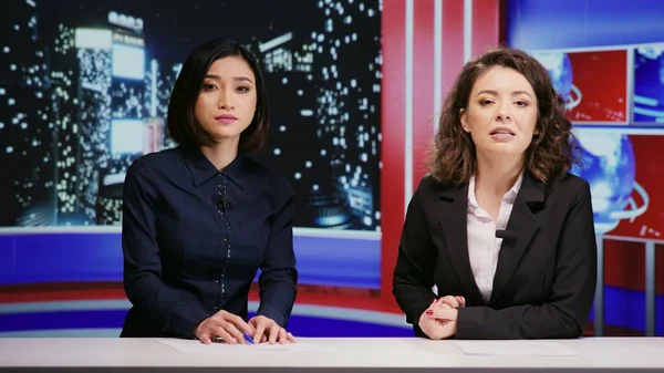 Diverse journalists host night show live on tv network, presenting breaking news segment in newsroom. Media presenters team addressing daily international events with television reportage.