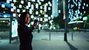 Asyalı iş adamı, gece yarısı şehir merkezinde sokak lambalarıyla mesajları kontrol ediyor. Neşeli insan tek başına gezinmekten zevk alıyor, yön bulmak için akıllı telefonu kullanıyor..