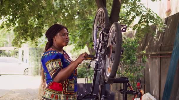 エネルギッシュな黒人女性の自転車タイヤを家庭の庭で微調整しました アクティブな女性の自転車を庭で修理し プロのツールで車両の毎年メンテナンスを行います — ストック動画