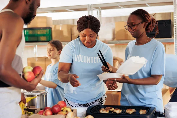 友好的黑人妇女快乐地为无家可归的美国穷人和穷苦的非洲男人提供免费食物 饥饿的 不那么幸运的男子从饥饿救济小组获得食物捐赠 — 图库照片