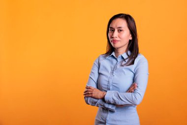 Mutlu model, sarı arka planda kolları bağlı bir şekilde stüdyoda duruyor. Kamera karşısında kendinden emin ve kaygısız. Neşeli Filipinli genç yetişkin doğal bir ifadeyle eğleniyor, boş zamanların tadını çıkarıyor.