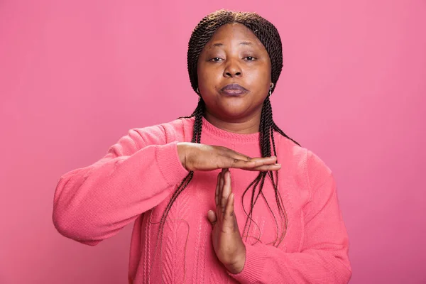 怒っている女性は ピンクの背景を持つスタジオで腕と休憩時間のサインを作るT字の手でタイムアウトジェスチャーを行います アフリカ系アメリカ人の若い大人の広告一時停止シンボル — ストック写真