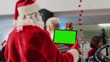 Noel süslü alışveriş merkezi çalışanı elinde tablet olan Noel Baba 'yı taklit ediyor, müşteriler etrafta dolaşırken, krom ekranda video izlemek için işe ara veriyor, kapatıyorlar.