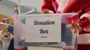 Noel tatilinde insani yardım için hazırlanan moda dükkanındaki bağış kutusunun yakın çekimi. Noel Baba kılığındaki işçi cömert müşterilerden gereksiz giysiler topluyor.