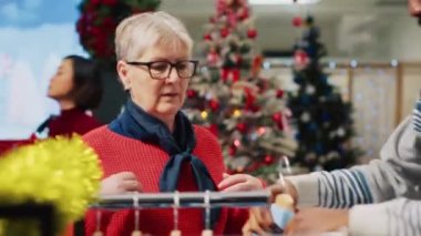 Noel süsleri mağazasında Noel Baba şapkası takan Afrikalı bir çalışan, Noel tatili sezonunda kararsız üst düzey müşterilerine alışveriş tavsiyesi veriyor.