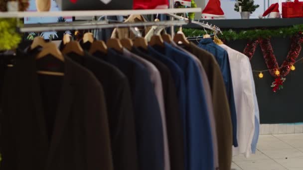 冬のホリデーシーズンの間にプレゼントを探している顧客を待っている空のクリスマスの装飾された衣料品店の正式な服のシャツのラック Xmasのブレザーはファッションブティックを飾る — ストック動画