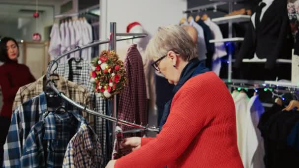 Äldre Kvinna Bläddrar Igenom Kläder Festlig Jul Dekorerad Shopping Köpcentrum — Stockvideo