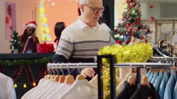 お祝いのファッションストアで服をブラウジング疲れた老人 クリスマスショッピングにうんざりした家族の贈り物を探して 甥のためのエレガントなブレザーをピッキングシニア顧客 — ストック動画