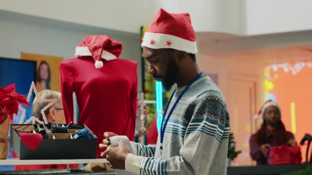 サンタの帽子をかぶったマネージャーは クリスマスの装飾された衣料品店で正式な服装のネックレスを配置します 冬季の休暇シーズンには クリスマス アデルンのショップでアクセサリーを検査する監督 — ストック動画