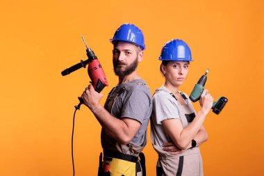 Elektrikli matkaplarla ayakta duran, kameraya bakan ve stüdyoda kendine güvenen kendine güvenen tamirciler. Tadilat ve yenilenme üzerinde çalışmak için ellerinde sondaj aletleri tutan inşaat ekibi..