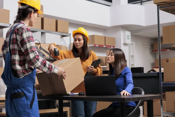 Asian warehouse workers team managing parcels shipping and receiving. Delivery employees checking pick ticket on laptop and scanning cardboard box barcode while working in storehouse
