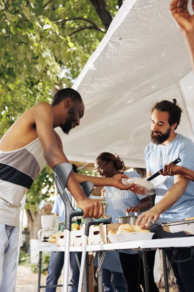 详细的形象 高加索男性志愿者提供免费食物给贫困的非洲裔美国人的拐杖 向穷人 残疾人和无家可归者提供饥饿救济的室外粮食银行 — 图库照片