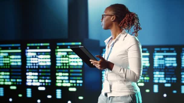 アフリカ系アメリカ人の専門家がサーバーの行を散策し さまざまなワークロードの処理リソースを提供しています 複雑な操作を解決するスーパーコンピュータを監視する経験豊富な女性 — ストック動画