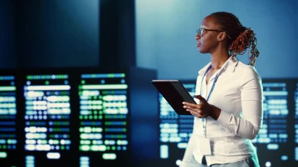 アフリカ系アメリカ人女性は さまざまなワークロードの処理リソースを提供するデータセンターシステムを歩いています 複雑な操作を解決するためのサーバーハブ機器の診断管理 — ストック動画