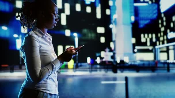 아프리카계 미국인 여성은 희미하게 거리를 산책하면서 스마트 사용하여 친구들과 채팅합니다 — 비디오
