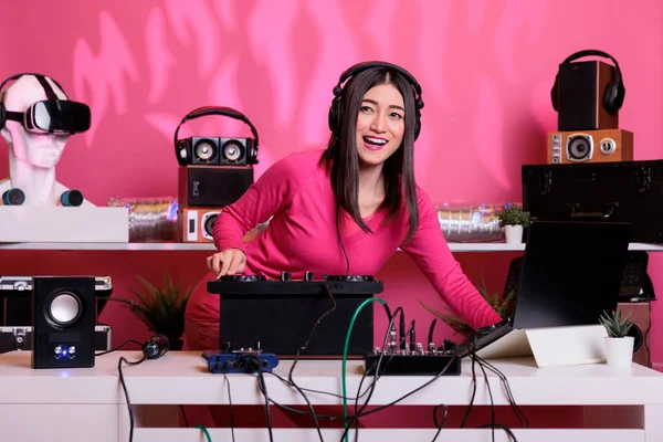 Asian musician playing electronic music using professional turntables while standing at dj table in studio over pink background. Artist doing performance at nightclub with audio equipment