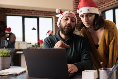 Şirket çalışanı, Noel arifesinde ofiste çalışırken dizüstü bilgisayardan proje yöneticisine görev sorunu gösteriyor. Noel Baba şapkalı iş arkadaşları şenlikli iş yerinde beyin fırtınası yapıyor ve çalışıyorlar.