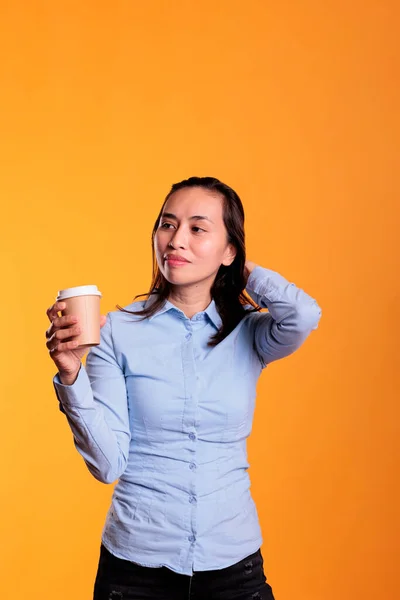 菲律宾妇女在演播室里摆姿势 端着一杯咖啡 享受着黄色背景下的热饮料 积极的成年人拿着纸杯 用饮料来保持精力和精神 — 图库照片