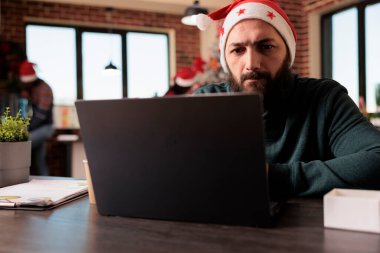 Süslü festival ofisinde dizüstü bilgisayarla çalışırken Noel Baba şapkası çözme problemine odaklanmış bir çalışan. Yılbaşı tatilinde iş yükünü yöneten düşünceli bir şirket çalışanı.