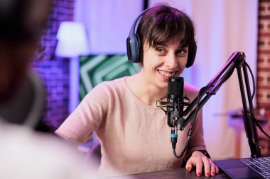 Cohosts streaming social media podcast with professional equipment, using vlogging camera and microphone to live broadcast conversation on internet channel. Women meeting in home studio to film show clipart