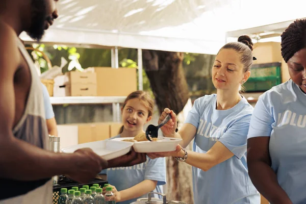 Aid organization recruits a diverse team to distribute free food, supporting less privileged and homeless people, in an effort to alleviate poverty. Volunteer women feed hungry african american man.