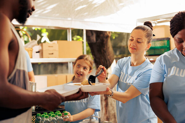 Aid organization recruits a diverse team to distribute free food, supporting less privileged and homeless people, in an effort to alleviate poverty. Volunteer women feed hungry african american man.