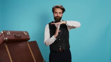 Otel kapıcısı stüdyoda mola sembolü yapıyor, otel ve turizm sektöründe çalışmak istiyor. Resmi kıyafetli şık bir kapıcı. Elleriyle duraklama hareketi yapıyor. Profesyonel bir iş..