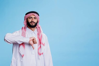 Geleneksel kıyafetler giymiş Müslüman bir adam kendinden emin bir ifadeyle ayakta duruyor ve portreyi aşağı çekiyor. Ciddi Arap pozu. Anlaşmazlığı işaret ediyor ve kameraya bakıyor.