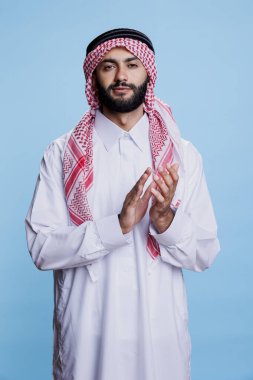 Geleneksel bornozlu kendine güvenen Arap adam stüdyoda ayakta alkışlıyor. Müslüman bir insan İslami kıyafetler giyiyor, alkışlıyor, destek veriyor ve kameraya bakıyor.