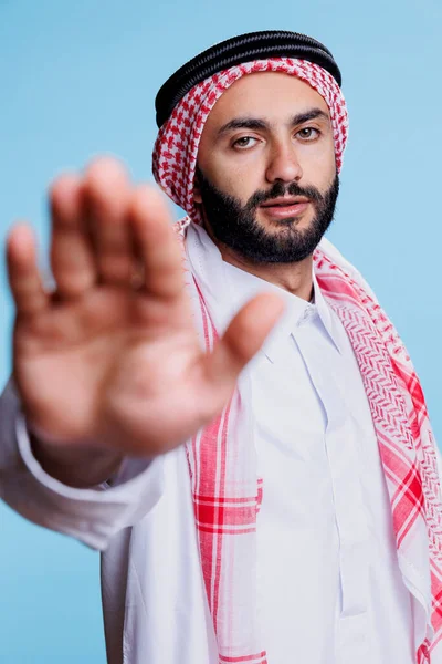 自信的穆斯林男子用手掌和镜头制作禁止停车标志 身着传统服装的严肃的阿拉伯男子以手绘肖像表示拒绝姿态 — 图库照片