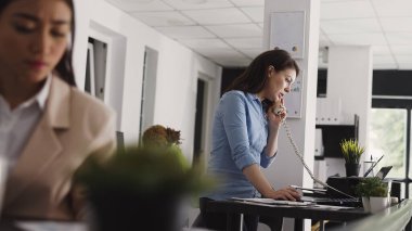 Şirket çalışanı sabit hattan konuşuyor ve yeni proje yatırımları üzerinde çalışıyor. Girişimci ofis kablosu telefonuyla birlikte çalışma alanında uzaktan sohbet ediyor. Üçayak atışı.