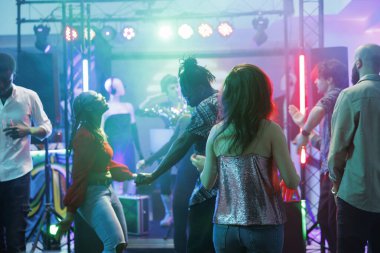 Parti dansçıları dans pistinde dans ederken gece kulübünde eğleniyorlar. Diskoteğe katılan ve dans eden insanlar sahne ışıklarıyla aydınlatılmış kulüpte müzik dinliyorlar.