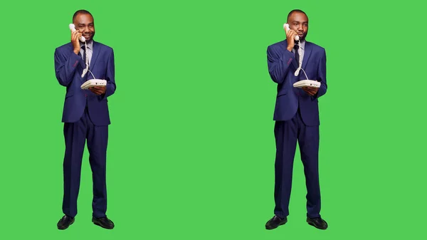 Confident employee answering landline phone call, having remote conversation on office telephone line with cord in studio. Male manager talking on phone, full body green screen.