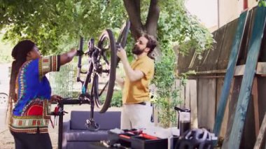Bahçede spor düşkünü sevgili ve sevgili, bisiklet lastiklerini, yıllık bakım için iş aletleriyle değiştiriyorlar. Sağlıklı çok ırklı çiftler, dışarıda bisiklet sürmek için bisiklet teçhizatını kontrol edip onarıyor.
